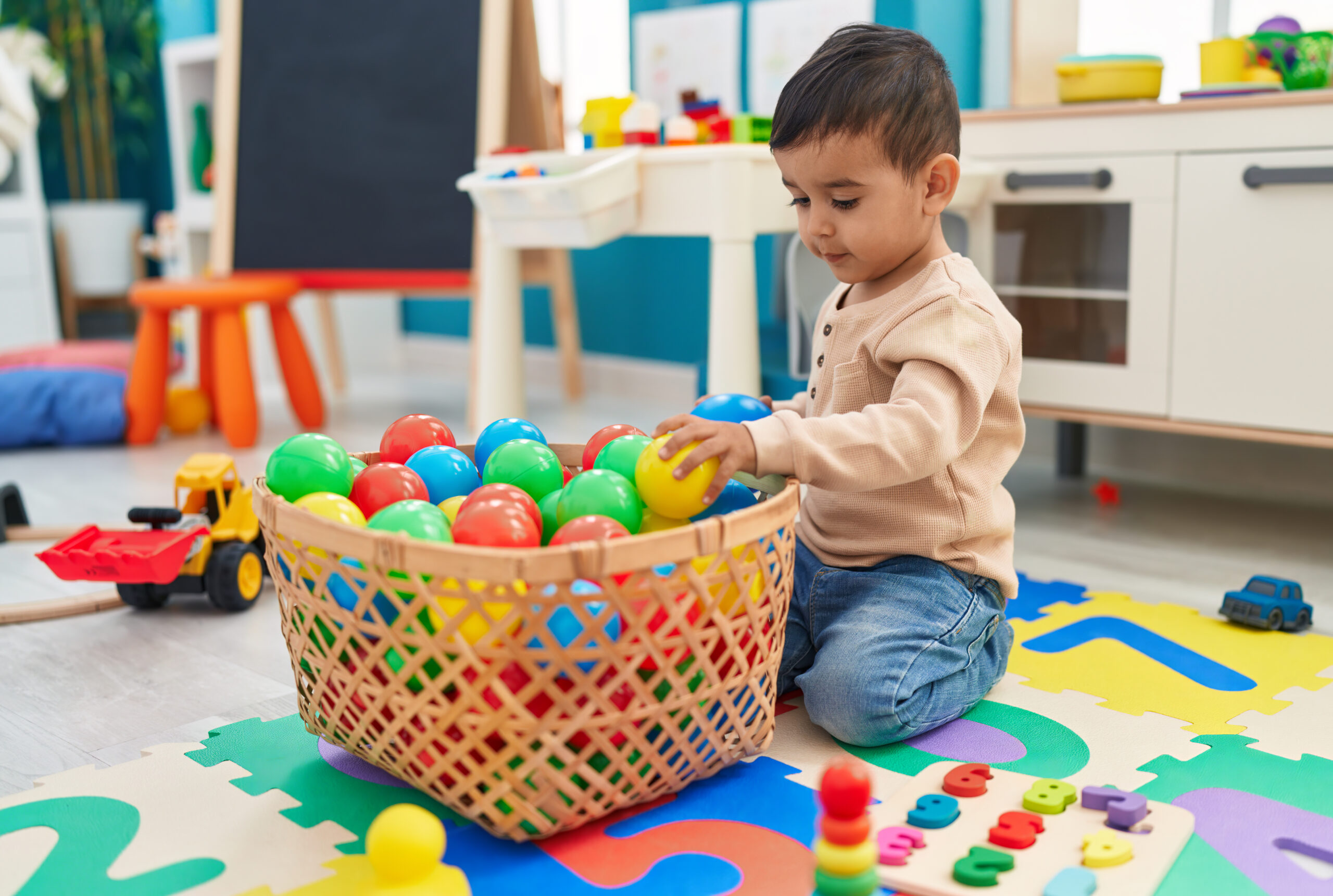 adorable hispanic toddler playing with balls sitting floor kindergarten scaled