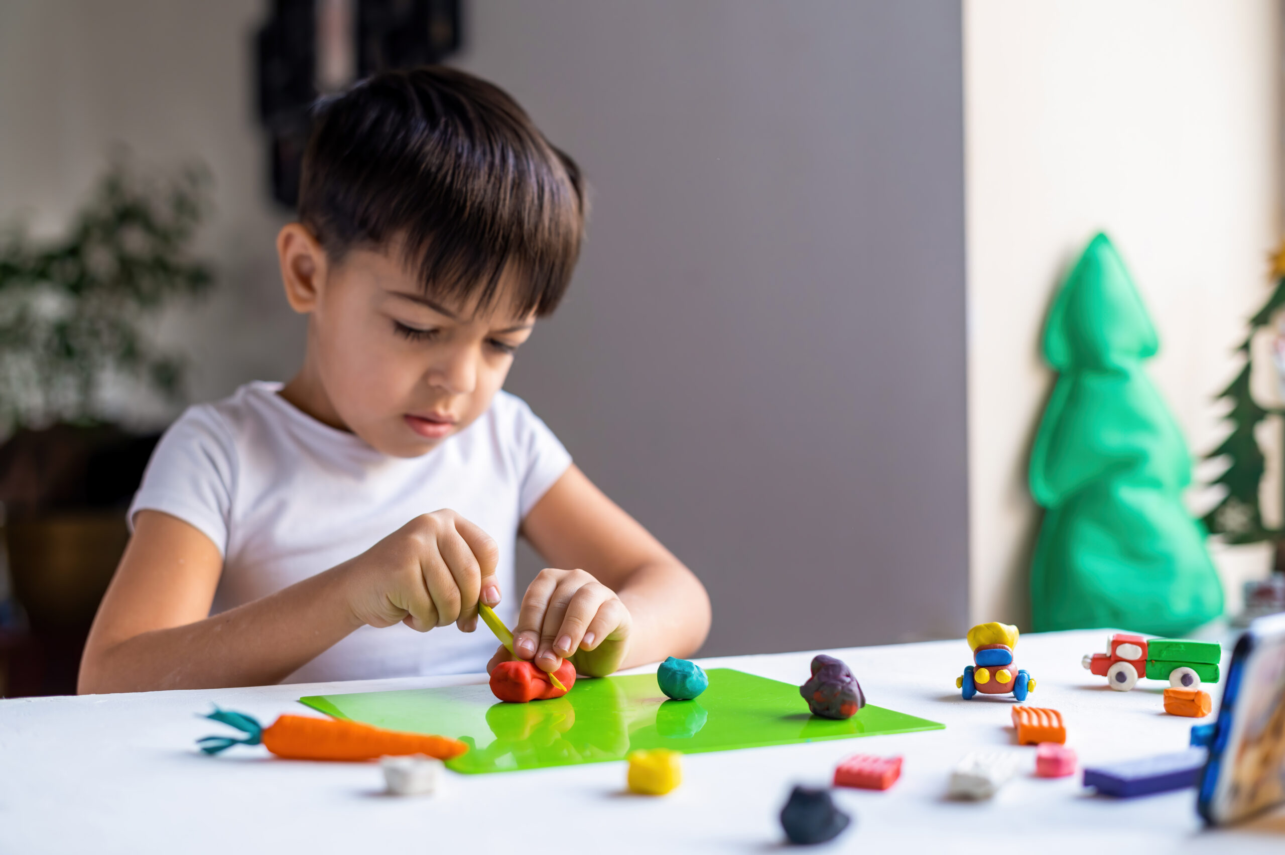 small caucasian boy playing with colored plasticine making figures white table happy child idea scaled